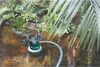 A submersible pump is operating in a pond or water feature, surrounded by lush greenery and palm fronds. Anteprima dell’immagine prodotto