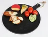 A round black serving board with various food items arranged on it, including cheese, bread, tomatoes, and cucumber slices. Anteprima dell’immagine prodotto