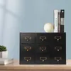 A black wooden organizer with nine drawers sits on a wooden desk, with books and a decorative sphere on top. A plant is visible to the left. Podgląd zdjęcia produktu