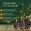 Three pine cone shaped LED candles with flickering flames are displayed on a wooden surface, with a blurred background of a Christmas tree and lights. Produktbild-Vorschau