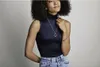 A woman wearing a dark blue sleeveless turtleneck and blue jeans, adorned with Pandora jewelry. Podgląd zdjęcia produktu