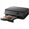A black Canon Pixma printer is shown from a diagonal front-left perspective, with a printed page emerging from the paper output tray. Náhled obrázku produktu