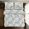 A top-down view of a neatly made bed with a floral patterned duvet and pillows, placed on a wooden floor next to a rug and a plant. Produktbild-Vorschau