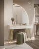 A white vanity table with gold legs and a semicircular mirror, featuring a green ottoman in front. Decorative items are on the table, and crystal pendant lights hang overhead. Produktbild-Vorschau