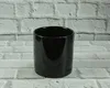 A black cylindrical object, likely a pot or container, is centered against a white brick wall background. Produktbild-Vorschau
