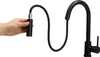A hand holding the spray head of a black kitchen faucet with a pull-out hose, against a white background. Náhled obrázku produktu