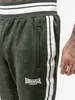 Close-up of a person's leg wearing green track pants with white stripes and a Lonsdale London logo. Náhled obrázku produktu
