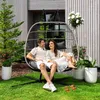 A couple relaxing in a hanging chair on a lawn in front of a modern house. Produktbild-Vorschau