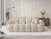 A cream-colored sofa with a ribbed texture is shown in a well-lit, minimalist living room setting. Produktbild-Vorschau
