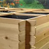 Close-up of a wooden raised garden bed with a black liner, set outdoors with blurred greenery and flowers in the background. Produktbild-Vorschau