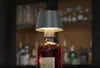 A lamp made from a liquor bottle sits on a bar counter, with shelves of bottles in the background. Produktbild-Vorschau