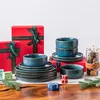 A collection of blue ceramic dishes and red gift boxes arranged on a wooden surface, with some greenery and small gift boxes. Náhled obrázku produktu