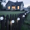 A string of solar-powered globe lights is attached to a wooden fence in front of a house. Produktbild-Vorschau