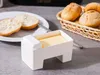 A butter dish with a lid and butter inside, next to sliced bread and a basket of rolls. Podgląd zdjęcia produktu