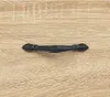 A close-up of a black drawer pull on a wood-grain surface. Podgląd zdjęcia produktu