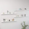 Four white wall shelves are mounted on a white wall, each decorated with various small decorative items. Náhľad obrázku produktu