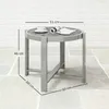 A round side table with a cup and magazine on top, placed on a stone patio with a brick wall in the background. Dimensions are indicated with lines and text. Produktbild-Vorschau