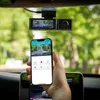 A hand holding a smartphone displaying a dashcam app, with the dashcam mounted on a car's windshield in the background. Produktbild-Vorschau