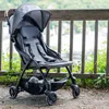 A stroller is placed on a dirt path next to a wooden fence, with greenery and a body of water in the background. Voir les images du produit