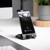 A wireless charging station is placed on a desk next to a computer monitor and a potted plant. Produktbild-Vorschau