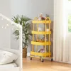 A yellow rolling cart filled with toys and decorative items sits next to a plant and a bed with string lights. Produktbild-Vorschau
