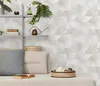 A shelf with decorative items and pillows on a couch, with a geometric patterned wallpaper in the background. Produktbild-Vorschau