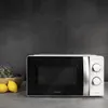 A white microwave oven with a black glass door is placed on a gray countertop, with a basket of lemons and lavender in the background. Anteprima dell’immagine prodotto