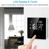 A hand is shown touching a digital thermostat mounted on a white wall, with a blurred background of a room interior. Podgląd zdjęcia produktu
