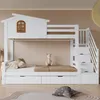 A white bunk bed with a house-shaped top bunk, a window, and stairs with drawers. It is set in a child's bedroom with a stuffed animal on the lower bunk. Produktbild-Vorschau