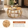 A round wooden coffee table with a curved frame base is shown in a living room setting with a fireplace and a sofa. The image also includes a circular inset showing a close-up of wood slices and text highlighting product features. Anteprima dell’immagine prodotto