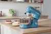 A blue stand mixer is on a kitchen counter next to a cake and strawberries. Produktbild-Vorschau