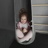 A young girl is sitting in a gray hanging chair. Produktbild-Vorschau