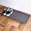 A grey shoe mat with two black and white sneakers on it, placed on a wooden floor next to a white wall. Náhled obrázku produktu