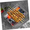 Silberner quadratischer Grillrost mit Fleischspießen über glühender Holzkohle, daneben eine Schale mit Limetten und Tomaten Anteprima dell’immagine prodotto