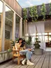 A woman sits on a wooden chair on a wooden deck, using a tablet. Produktbild-Vorschau