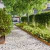 A garden path made of white gravel, bordered by green bushes and trees, with a corten steel edge. Náhľad obrázku produktu