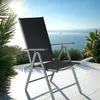 A black folding chair is placed on a white tiled patio overlooking a body of water with islands and mountains in the distance. Náhled obrázku produktu