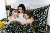 A mother is reading a book to her two young children in bed, under a duvet with a floral pattern. Podgląd zdjęcia produktu