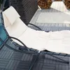 A close-up view of a beige cushioned lounge chair on a grey tiled patio, with a stack of firewood in the background. Voir les images du produit