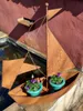A rusty metal sailboat planter with purple flowers sits by a pond. Produktbild-Vorschau