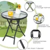 A round bistro table with a glass top and a folding metal frame, set in a garden with a house in the background. Inset images highlight features. Anteprima dell’immagine prodotto