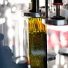 A close-up shot of a glass bottle filled with olive oil, part of an automated filling or packaging process. Produktbild-Vorschau