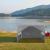 A grey pop-up tent is set up on a grassy area next to a lake, with hills in the background. Náhľad obrázku produktu