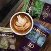 A cup of coffee with latte art is placed on a wooden surface, surrounded by coffee capsule packaging. Voir les images du produit