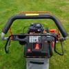 A close-up view of a lawnmower's handle and engine, set against a green grassy background. Produktbild-Vorschau
