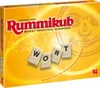 The image shows the front of a Rummikub board game box. The box is yellow with red lettering and features tiles with letters on them. Náhľad obrázku produktu