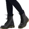 A pair of black Dr. Martens boots worn by a person. Voir les images du produit