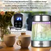 A glass electric kettle with colorful LED lighting is shown next to two beige mugs on a wooden table. A close-up inset shows the digital temperature display and control buttons of the kettle. Produktbild-Vorschau