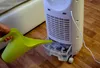 A person is pouring water into the water tank of a white air cooler using a green watering can. Náhled obrázku produktu
