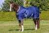 A brown horse wearing a navy blue turnout rug stands in a grassy field with trees and bushes in the background. Produktbild-Vorschau